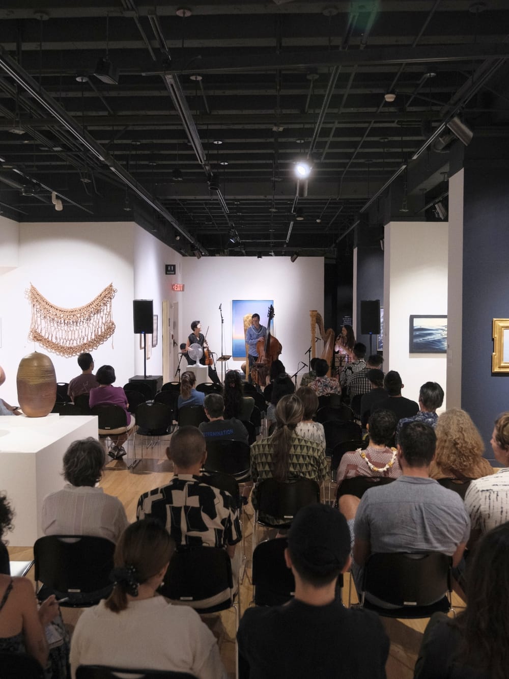 Audience seated for a Noise Cabinet performance in the galleries of Capitol Modern, musicians playing among the artworks